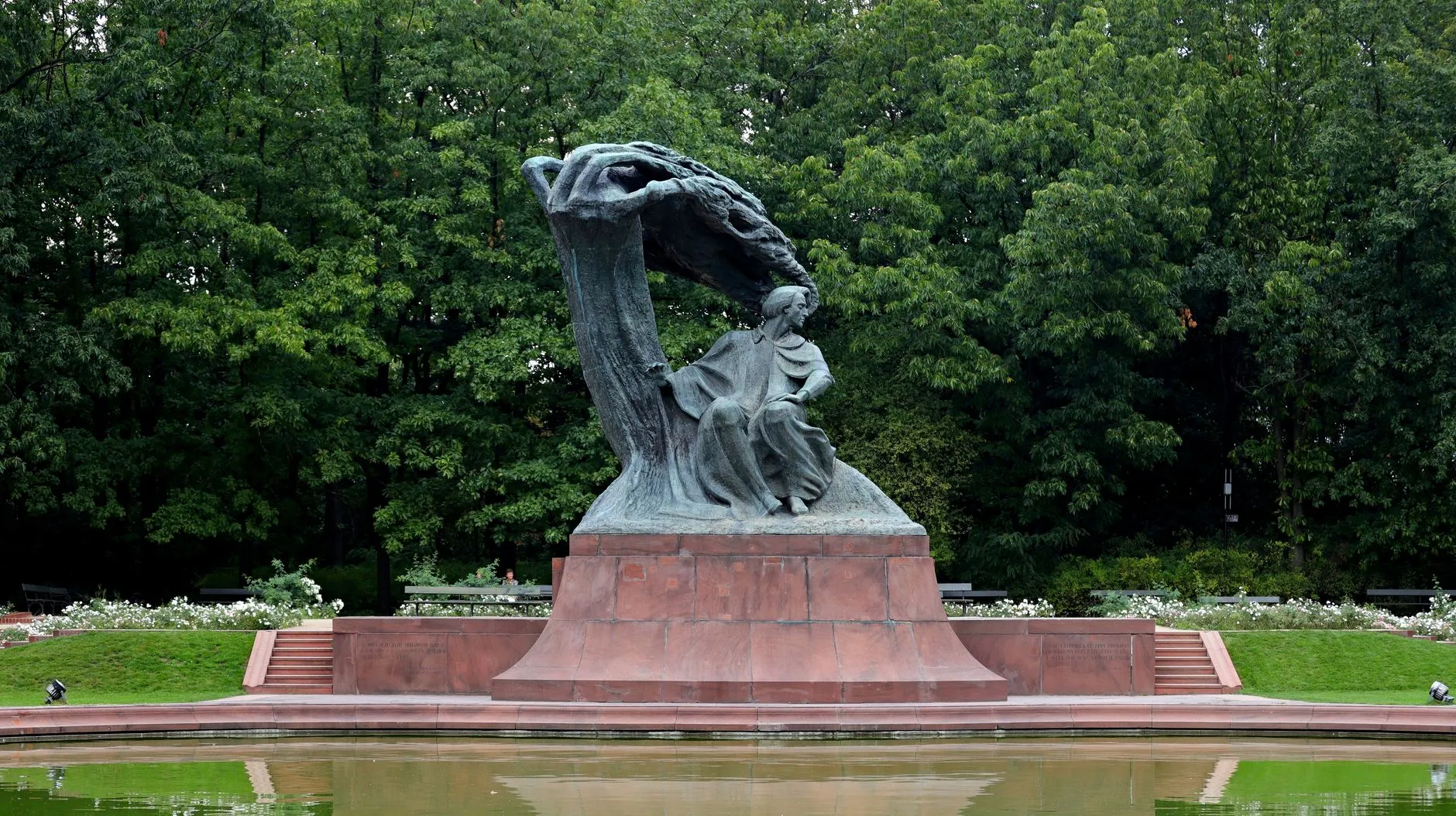 Pomnik Fryderyka Chopina w Łazienkach otoczony zielenią, z sadzawką na pierwszym planie