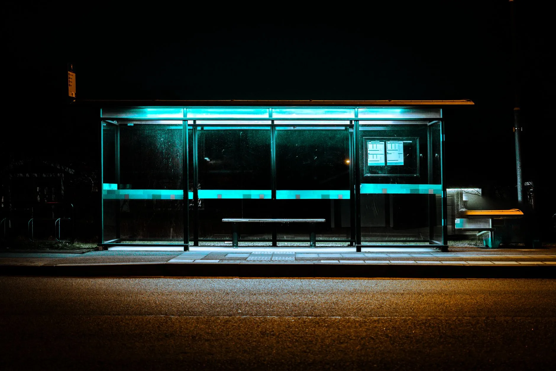 Pusty przystanek autobusowy nocą z podświetloną wiatą i ławką
