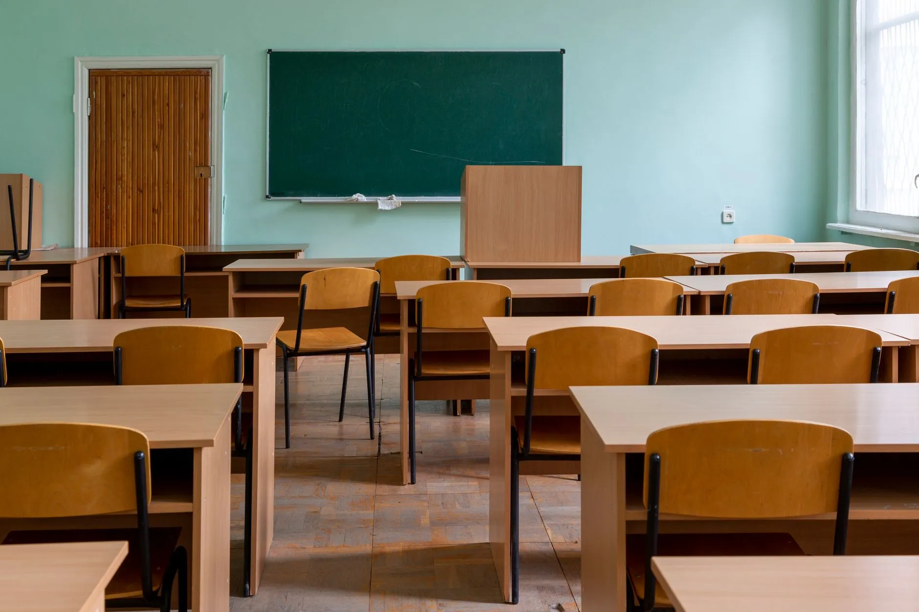 Pusta sala lekcyjna z drewnianymi ławkami, krzesłami i zieloną tablicą