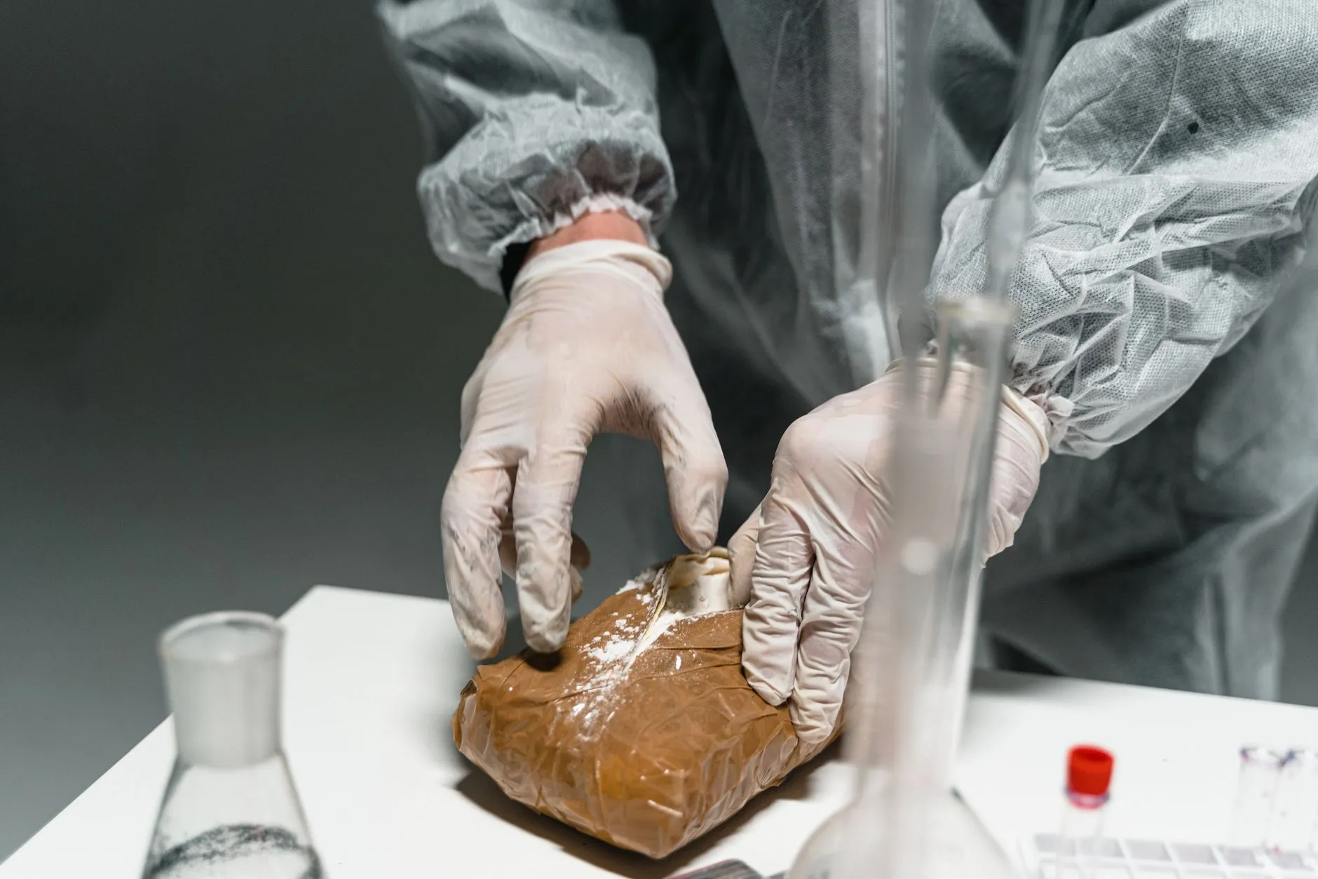 Dłonie w rękawiczkach otwierające paczkę z białym proszkiem na stole laboratoryjnym