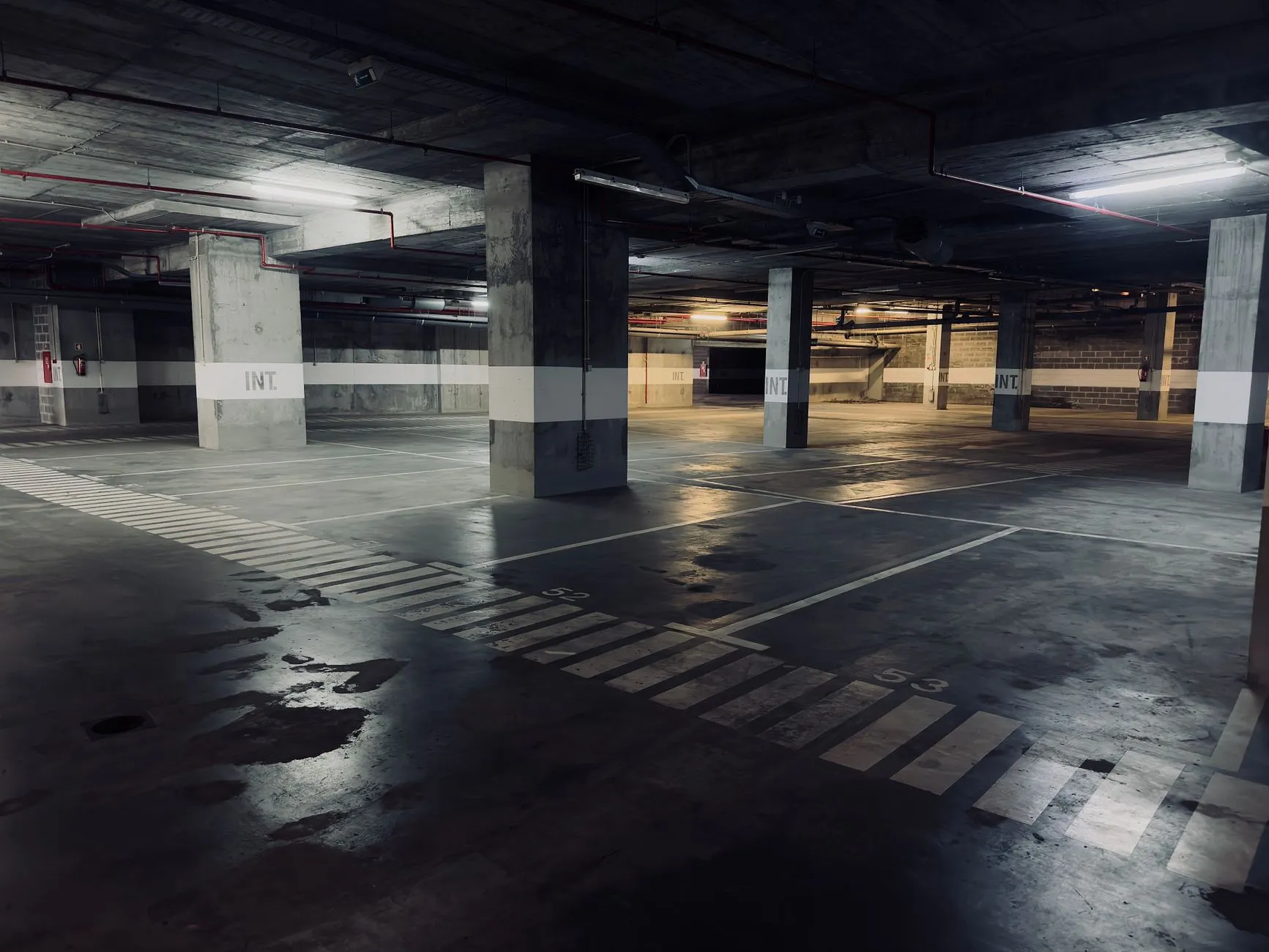 Pusty parking podziemny z betonowymi filarami i kałużami na posadzce