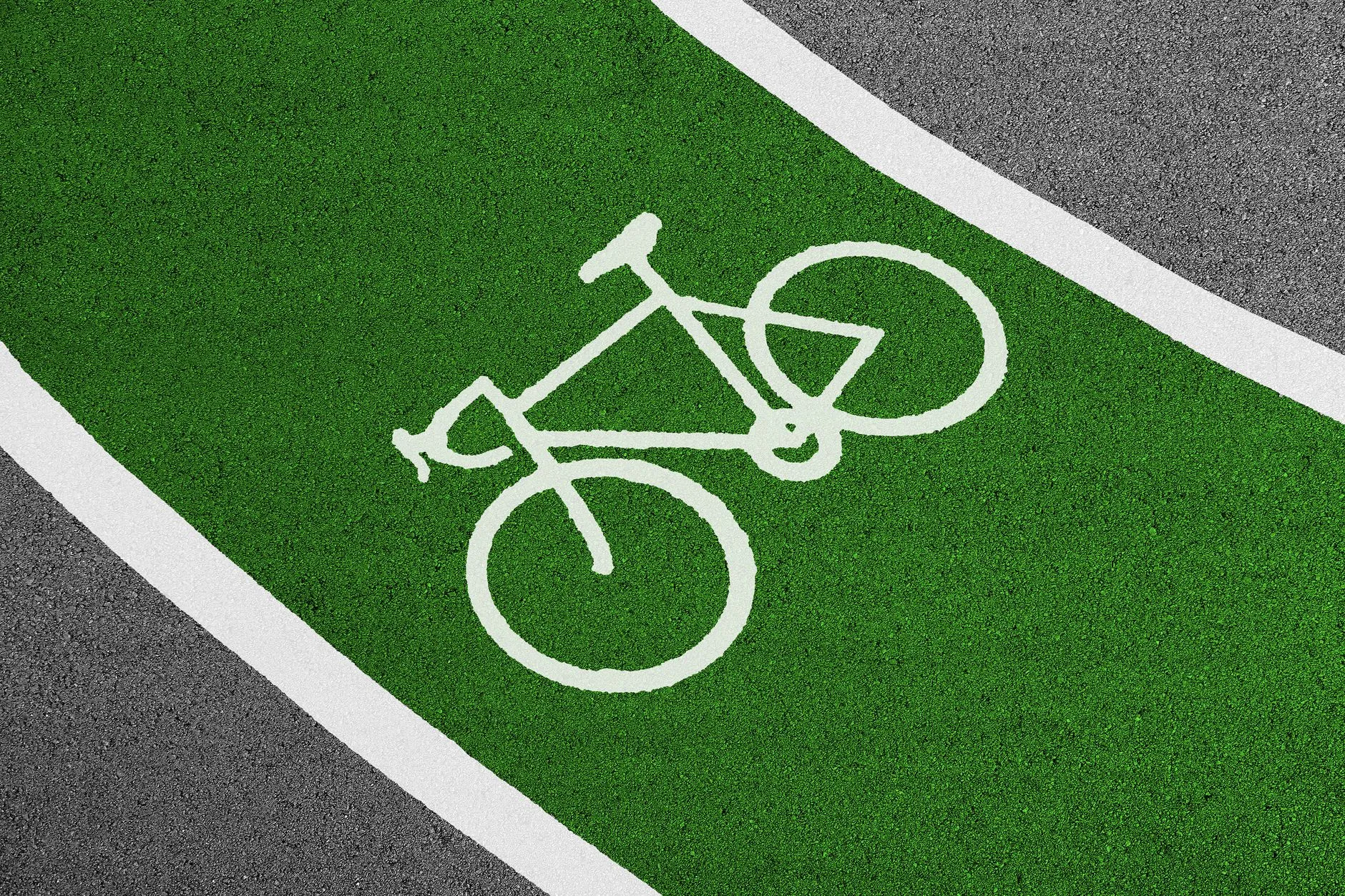 Biały symbol roweru na zielonej nawierzchni pasa rowerowego między białymi liniami