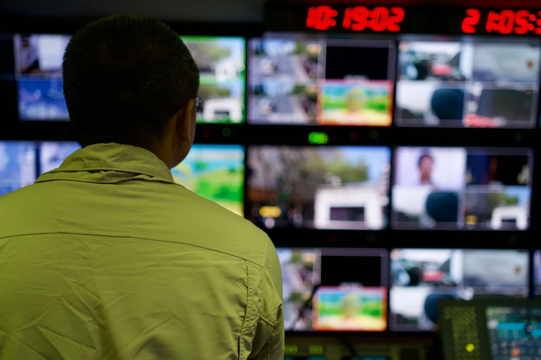 Mężczyzna widziany od tyłu przed ścianą monitorów w pomieszczeniu kontrolnym