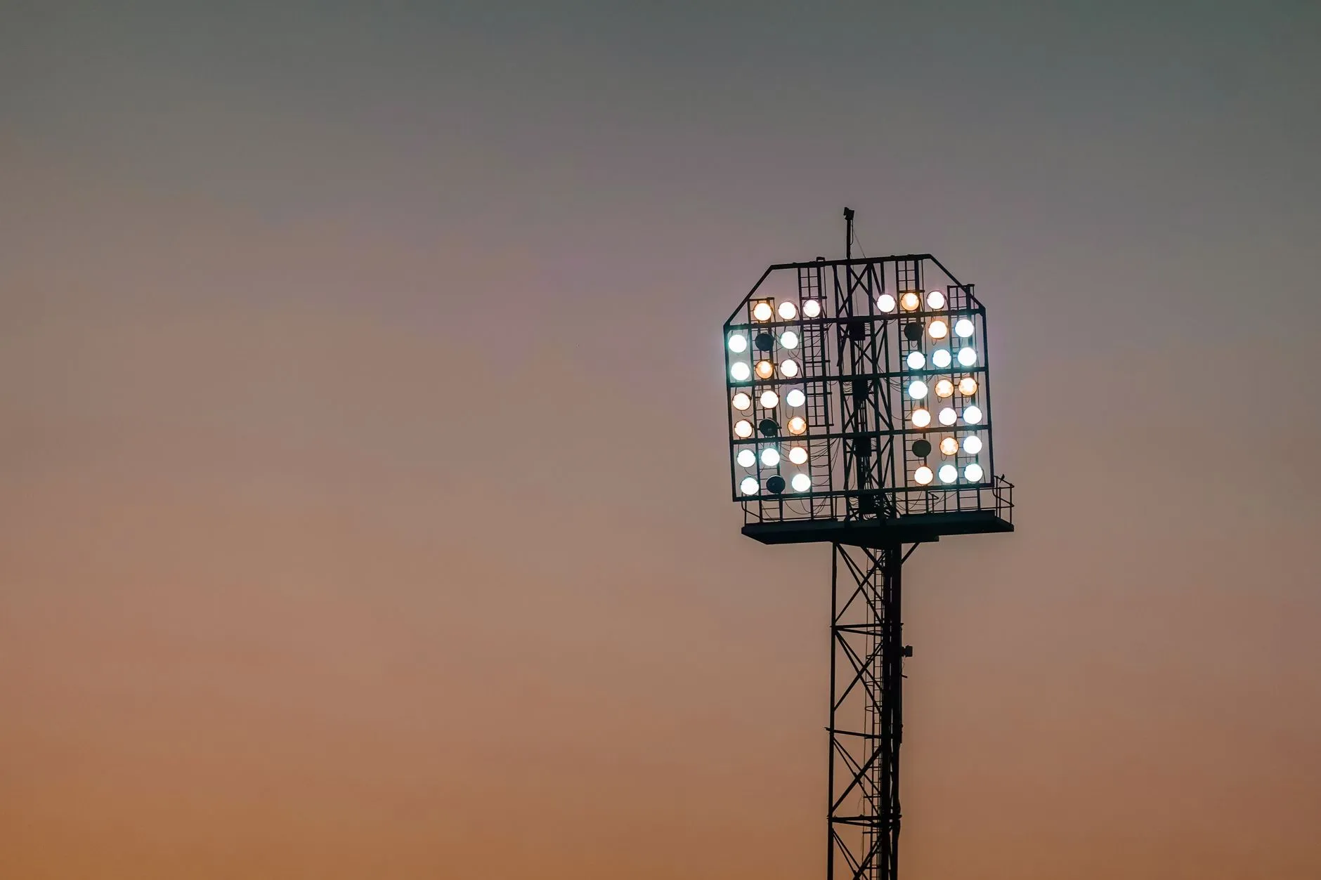 Zapalone reflektory na stadionowym maszcie na tle nieba o zmierzchu