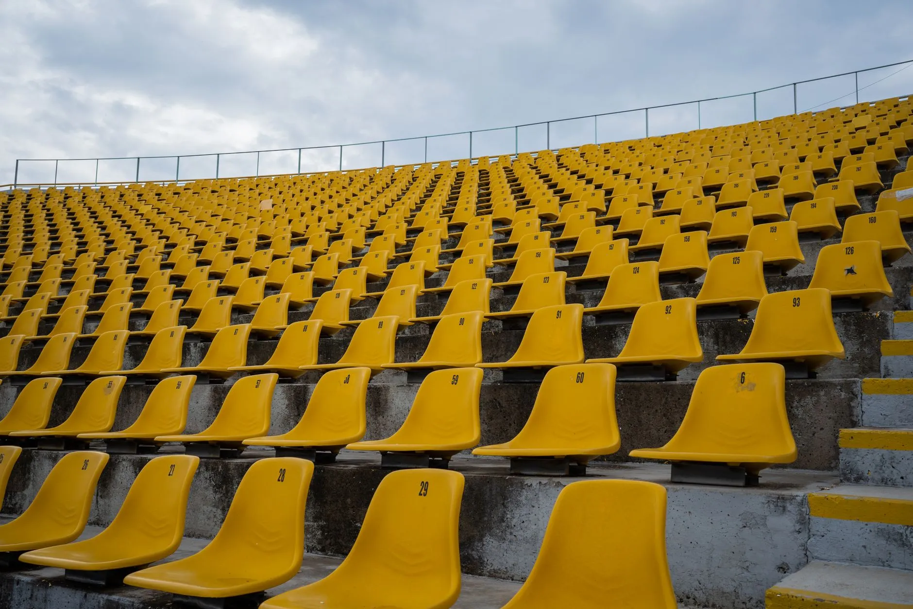 Rzędy pustych żółtych krzesełek na stadionowych trybunach pod pochmurnym niebem