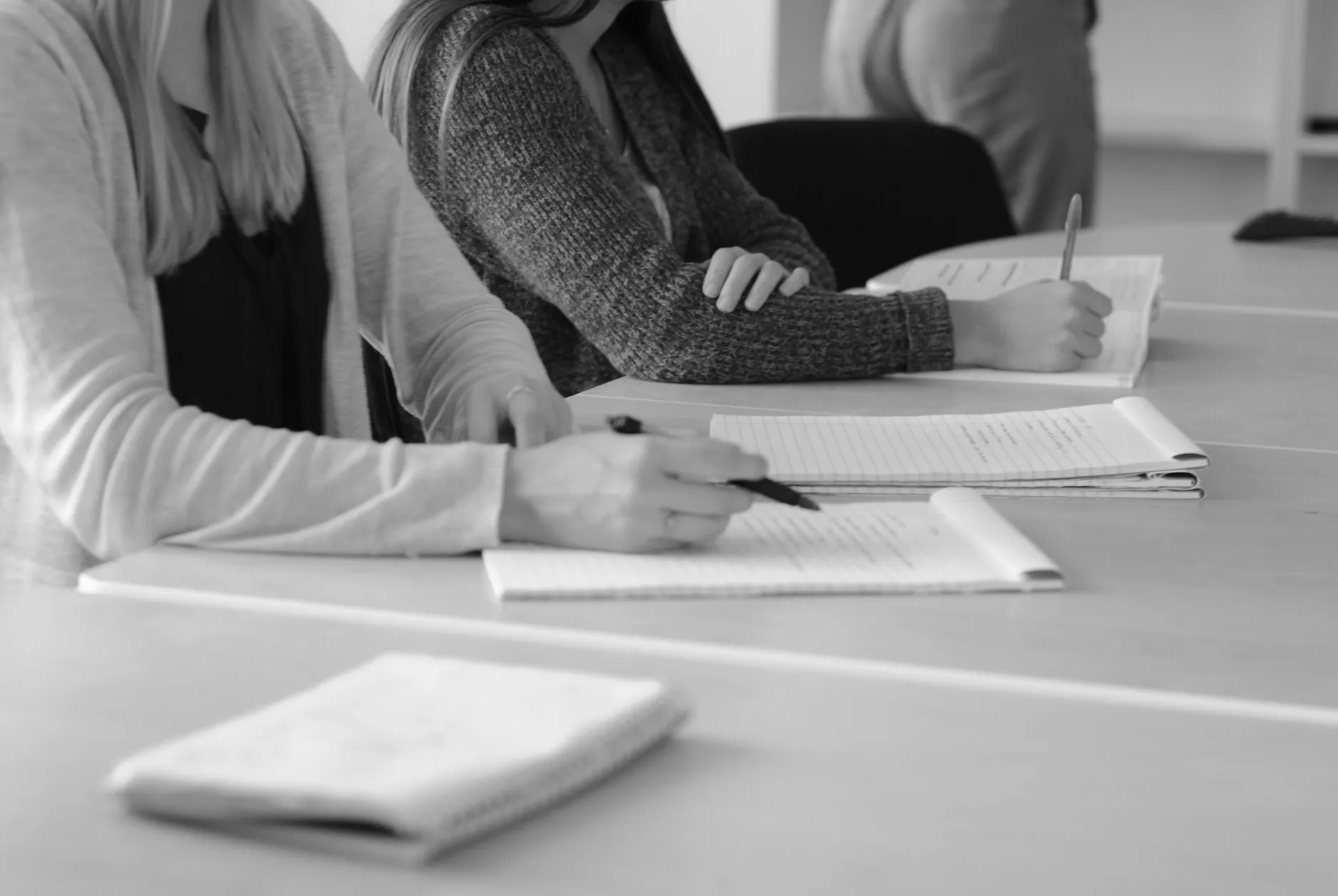 Osoby siedzące przy stole i zapisujące notatki w zeszytach