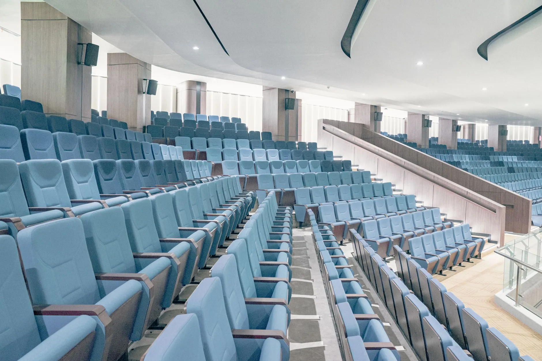 Pusta sala audytoryjna z rzędami niebieskich foteli i drewnianymi balustradami