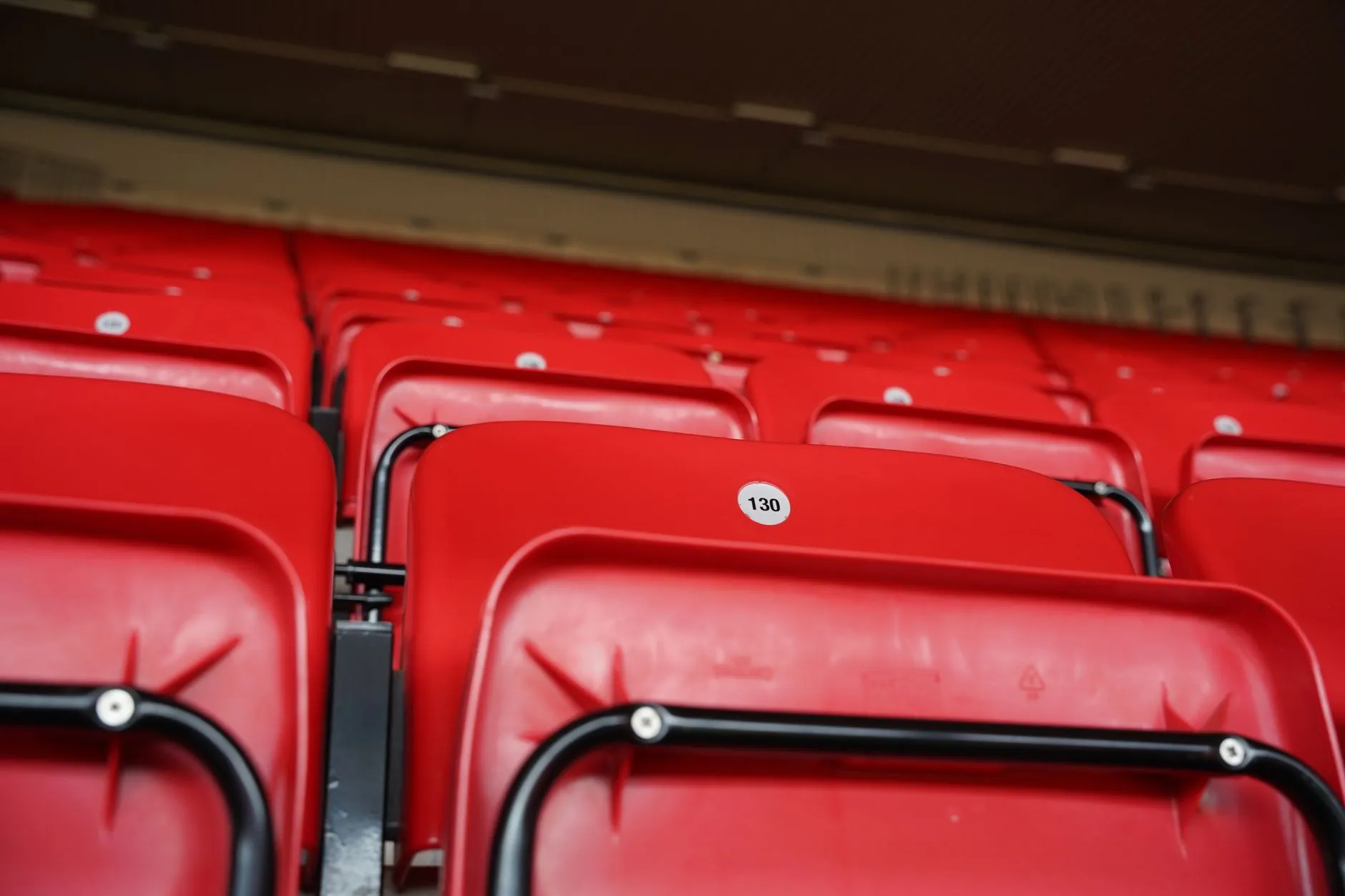 Rzędy pustych czerwonych krzesełek stadionowych z numerowanymi oparciami