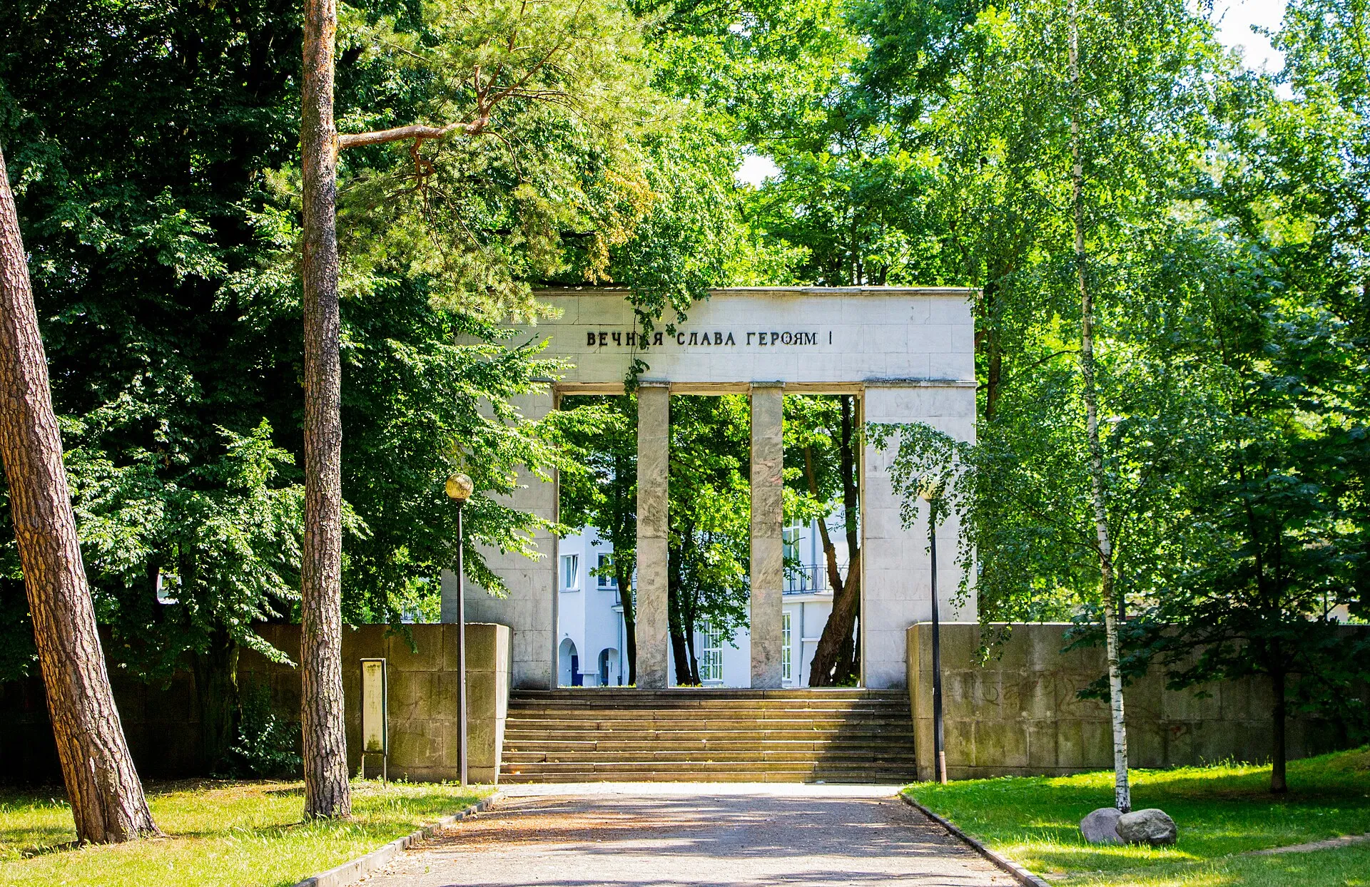 Brama cmentarza wojskowego w Kaliszu wśród drzew