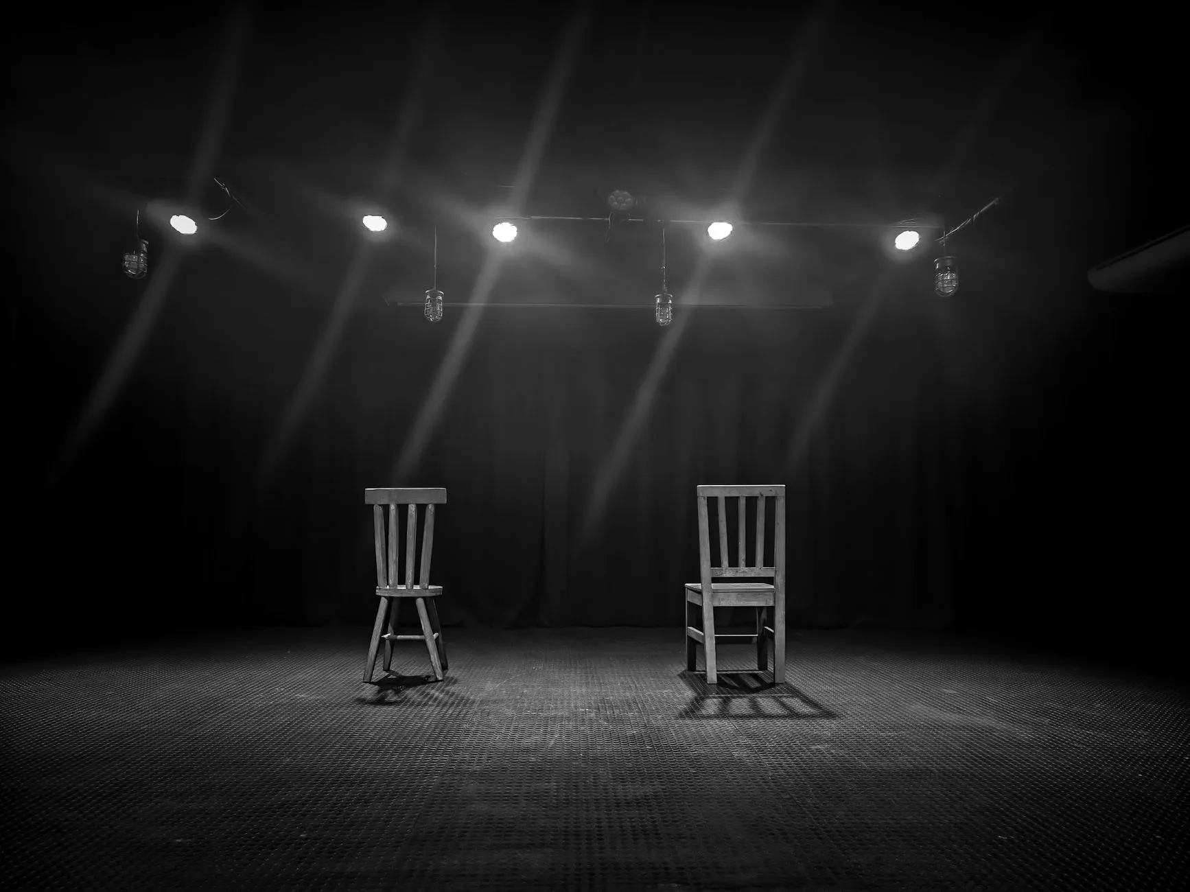 Dwa puste drewniane krzesła na scenie teatralnej oświetlonej reflektorami