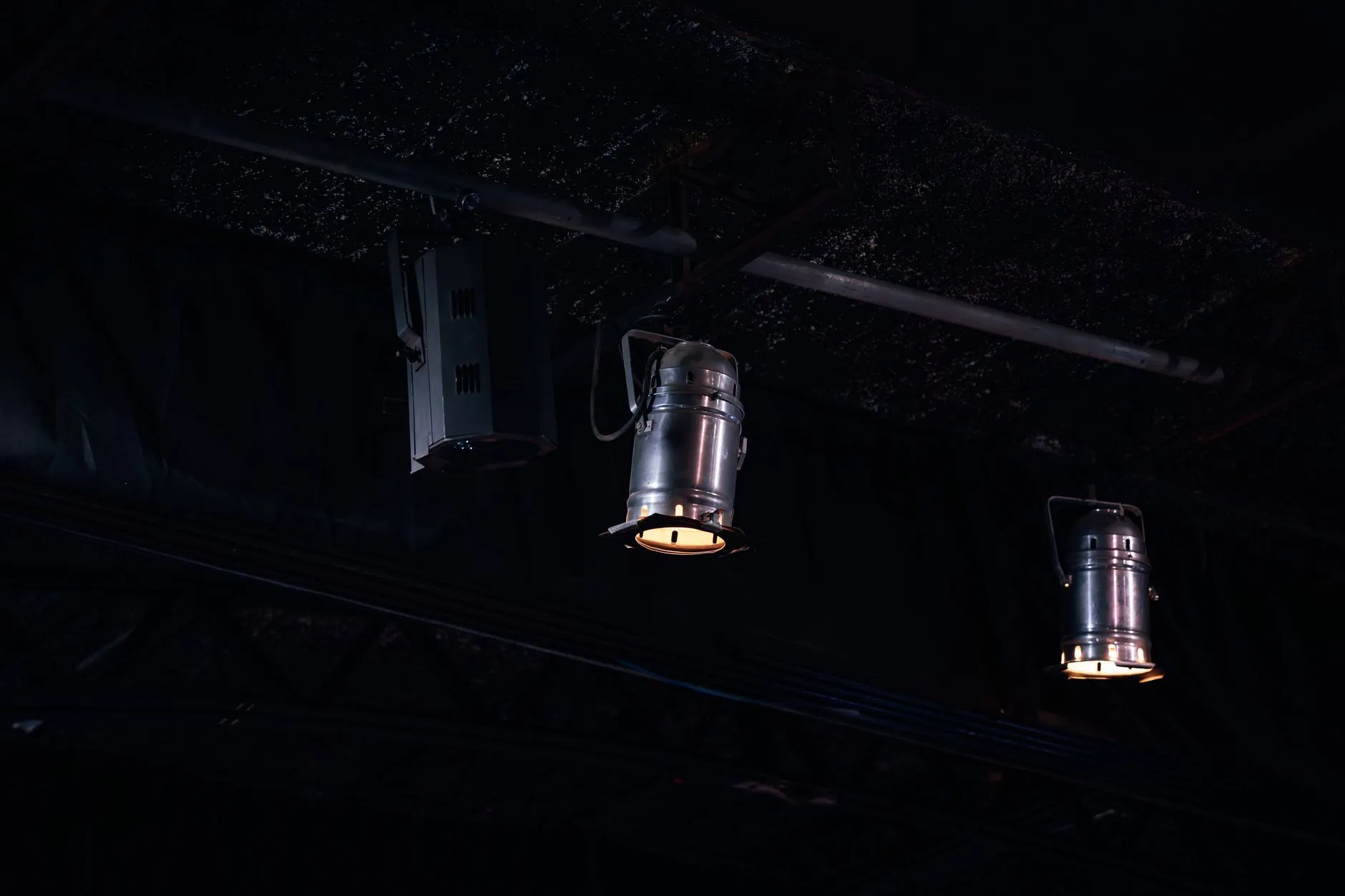 Metalowe reflektory zawieszone pod ciemnym sufitem, dwa emitują ciepłe światło