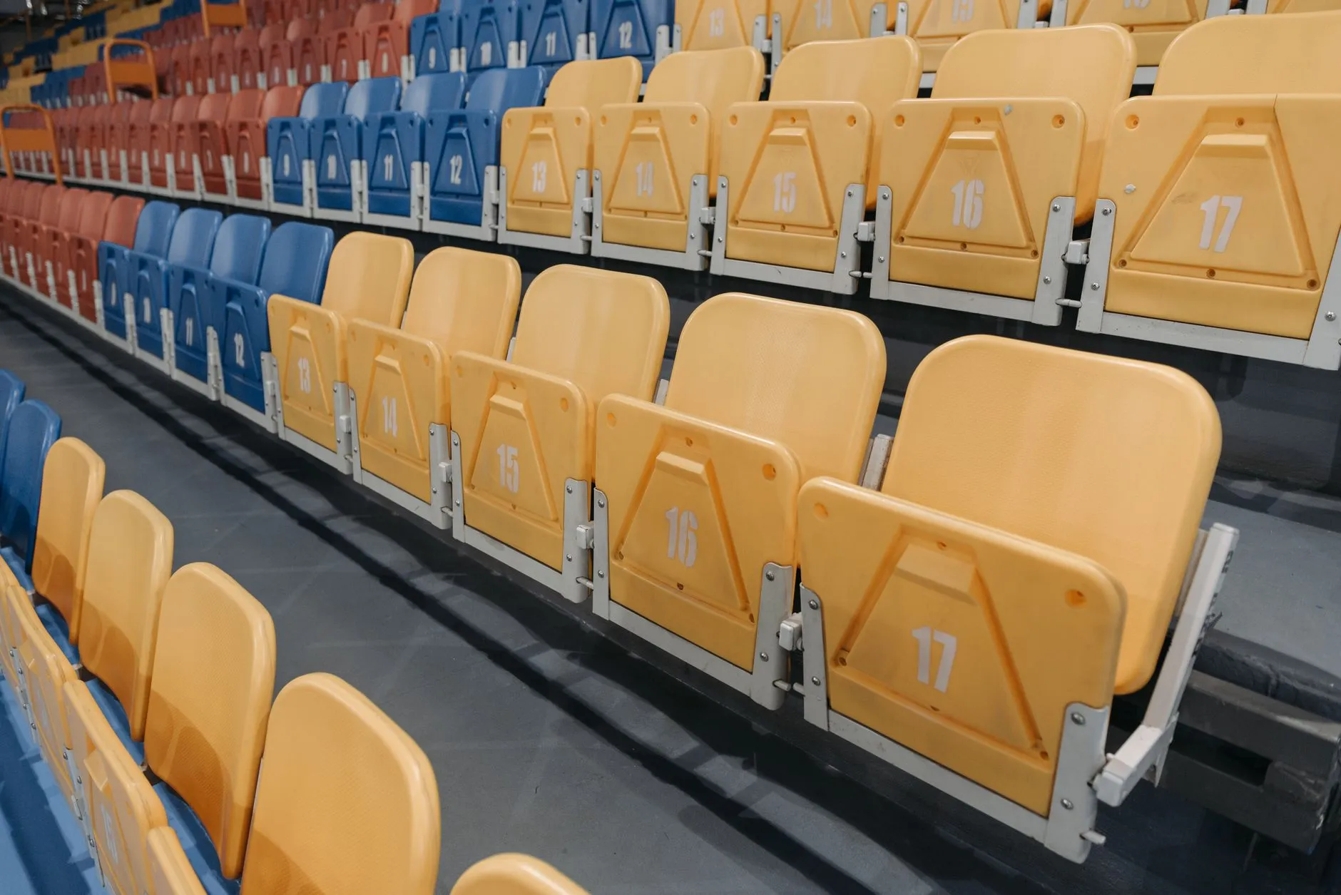 Rzędy pustych żółtych, niebieskich i czerwonych krzeseł na trybunach hali sportowej