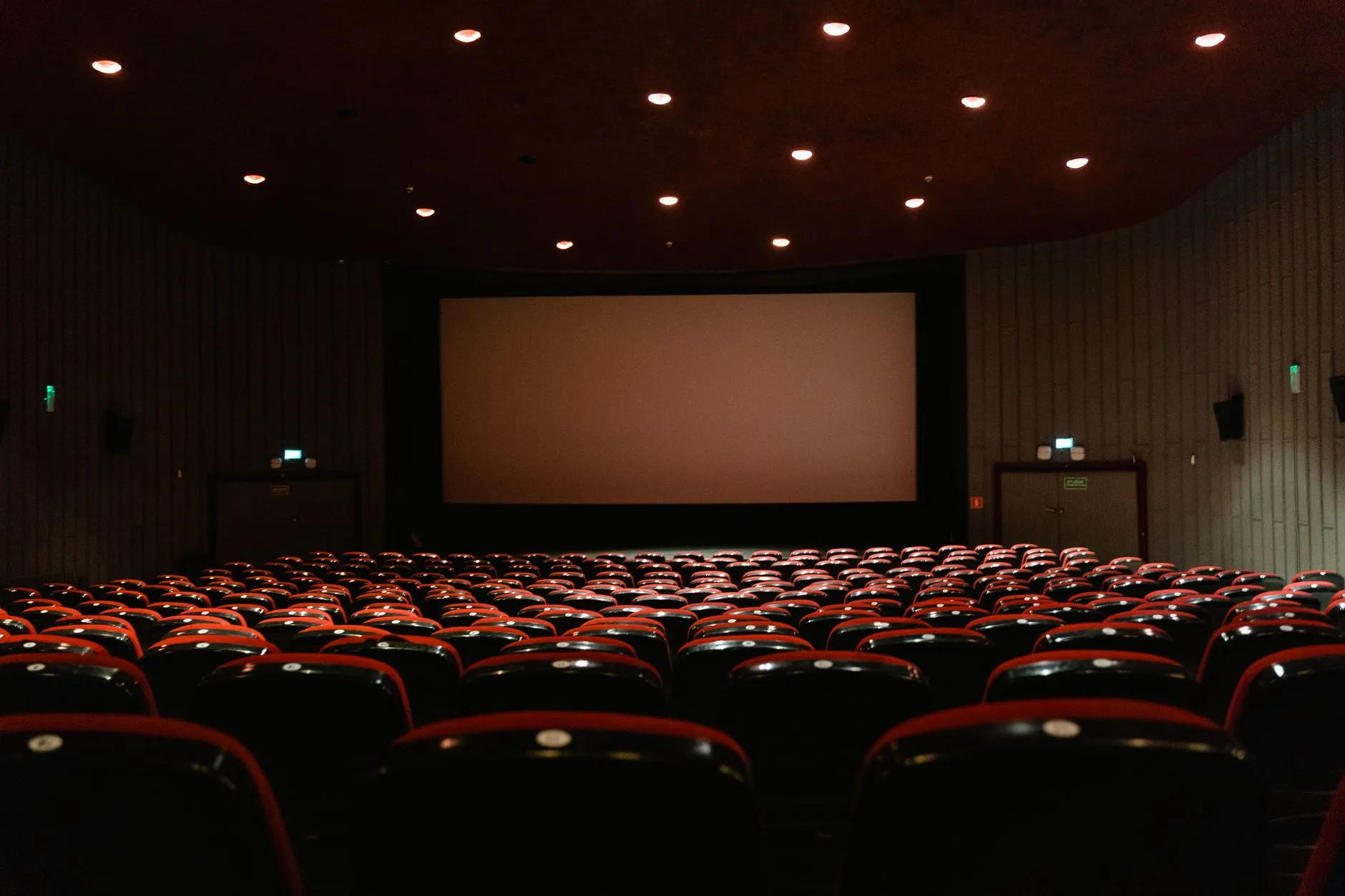 Pusta sala kinowa z rzędami czerwonych foteli przed dużym ekranem