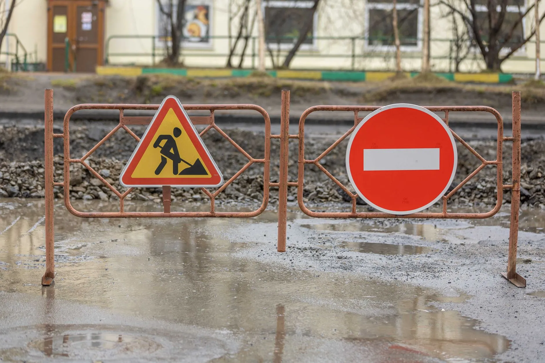 Metalowe barierki ze znakami robót drogowych i zakazu wjazdu na błotnistej drodze