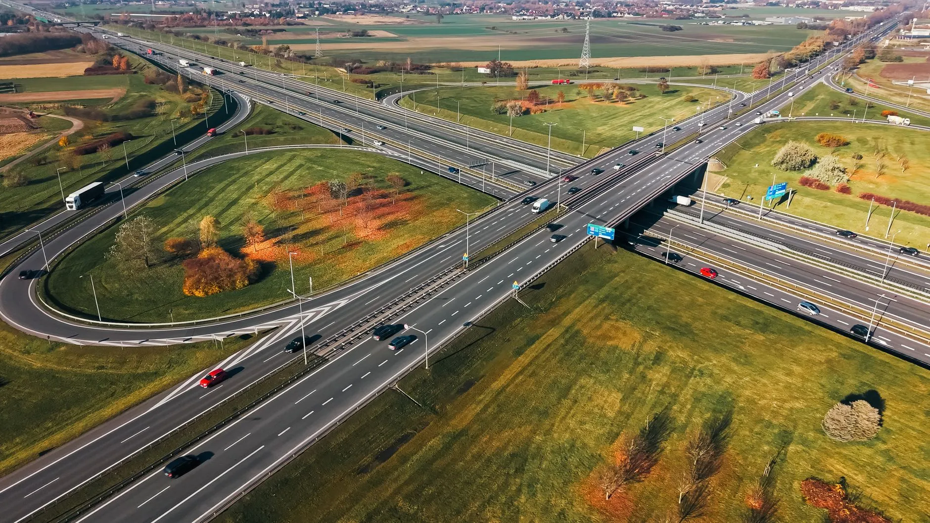 Wielopoziomowy węzeł drogowy z samochodami, otoczony polami i drzewami w jesiennych barwach
