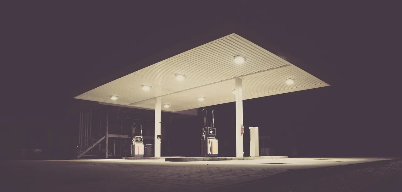Oświetlona stacja paliw nocą z dwoma dystrybutorami pod szerokim zadaszeniem