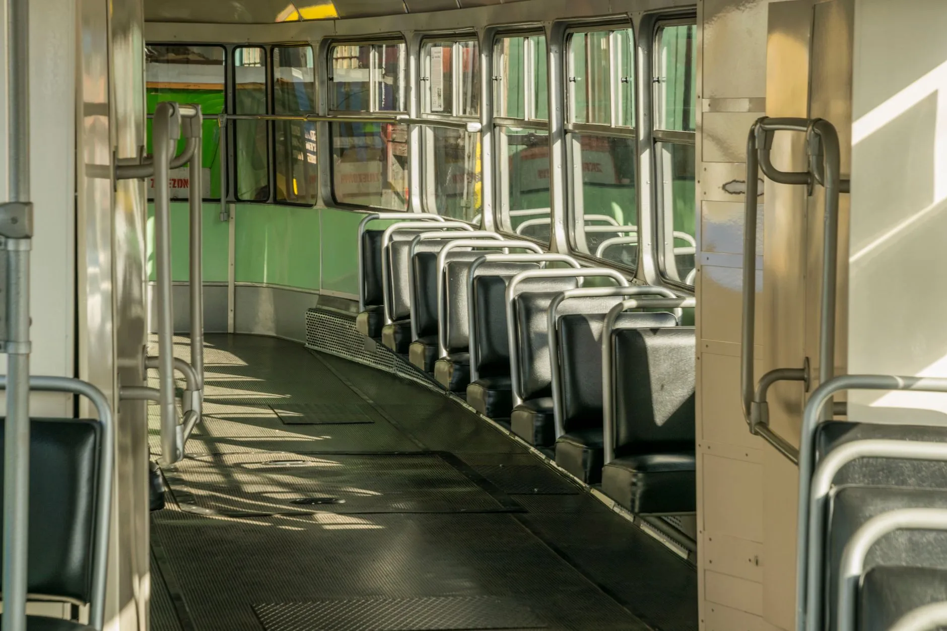 Puste wnętrze tramwaju z rzędami siedzeń i poręczami w świetle dziennym