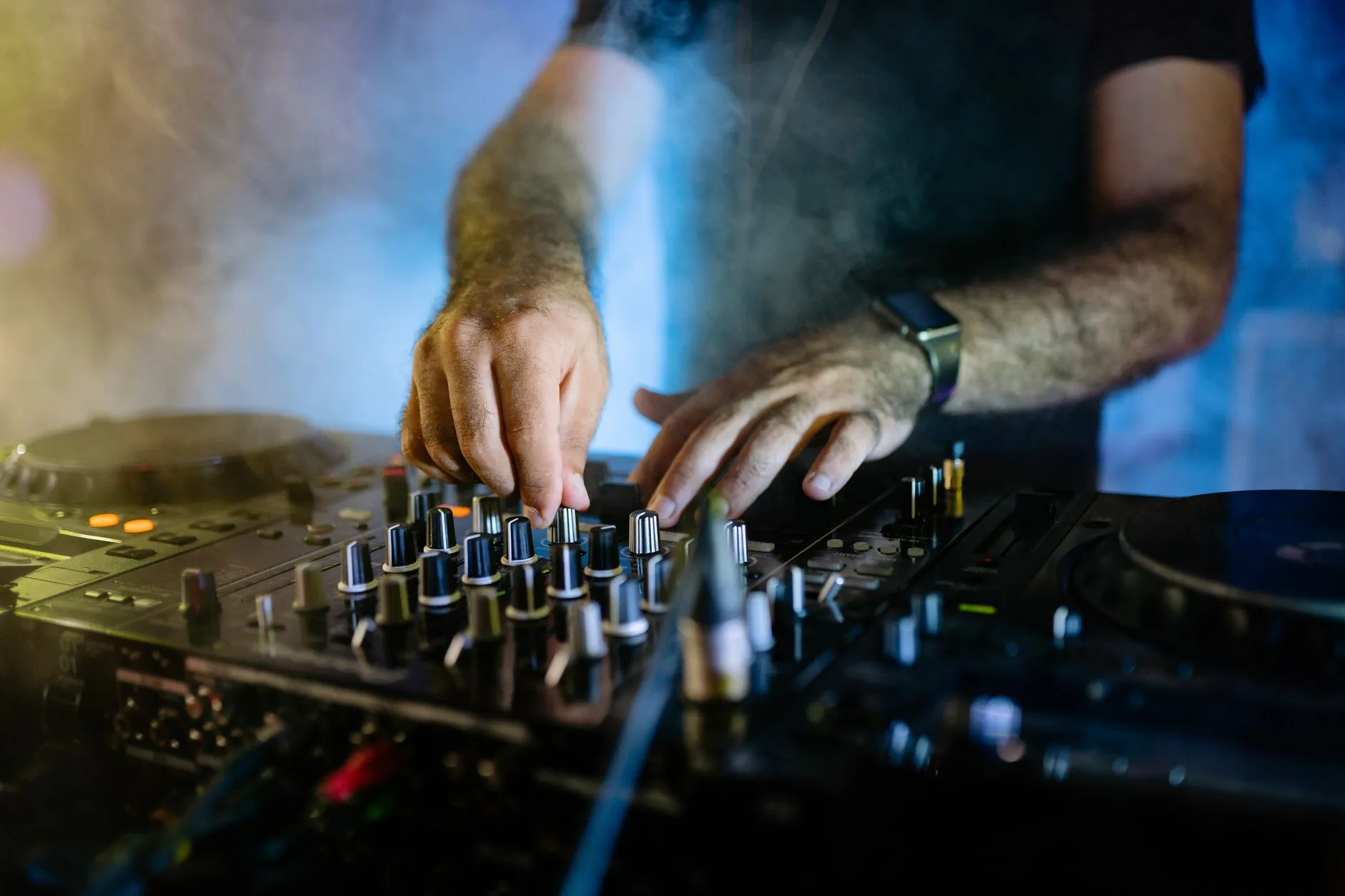 Dłonie DJ-a obsługującego konsoletę w niebieskim i żółtym oświetleniu
