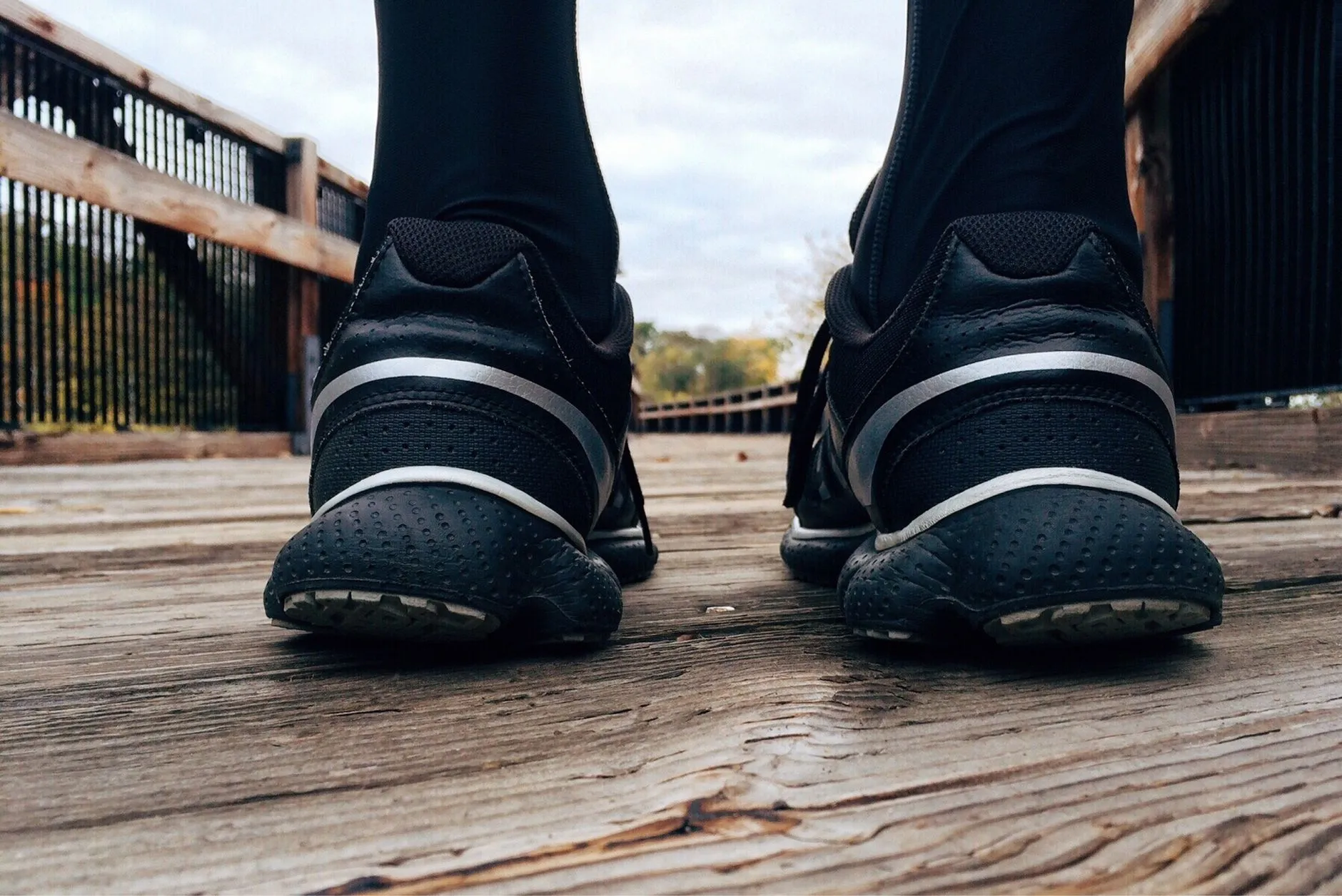 Czarne buty sportowe widziane od tyłu na drewnianym pomoście z balustradami