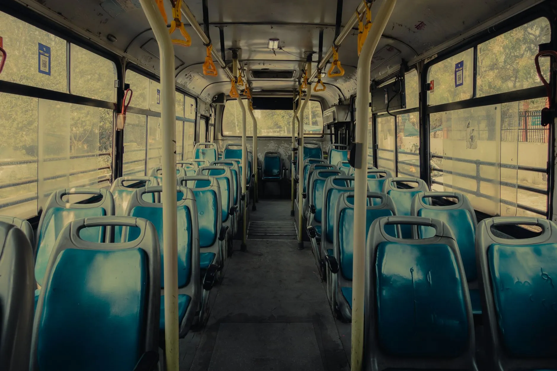 Puste wnętrze autobusu z niebieskimi siedzeniami i żółtymi uchwytami dla pasażerów